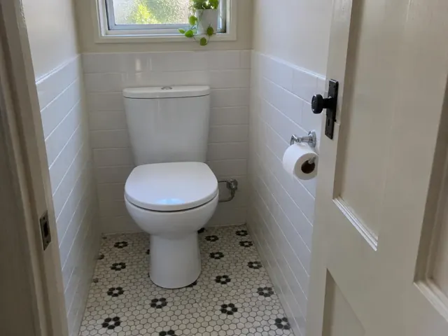 Clean white toilet in a small tiled bathroom with patterned floor and window in Gordon
