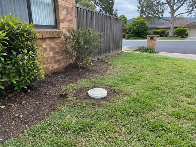 Capped drain inspection opening in a grassy front yard beside a brick house in St Ives