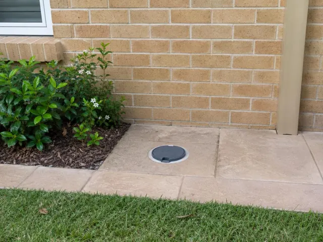 Capped access point set in tiled paving beside a brick wall and garden bed in Pymble