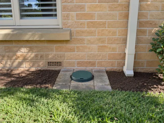 Capped sewer opening set in pavers beside a brick house wall and garden bed in Killara